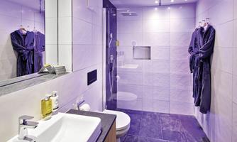 A modern bathroom with elegant furnishings. There is a shower, a sink, and two bathrobes hanging on the wall.