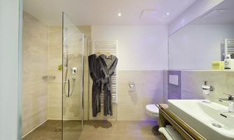 A modern bathroom with a shower and bathtub. An elegant bathrobe hangs on the wall.