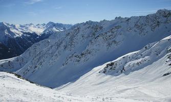 A snow-covered mountain landscape with steep peaks. The clear sky and bright sunshine create a beautiful winter atmosphere.