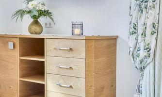A wooden cabinet with three drawers and an open compartment. At the top is a vase with flowers and a candle.