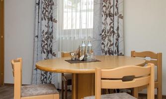 A simple dining area with a round wooden table and four chairs. Curtains with a floral pattern hang in front of a window.