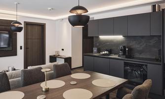 A modern kitchen with a dark color palette and elegant furniture. The dining area is cozy with a large table and stylish lamps.