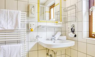 A modern bathroom with a sink, a large mirror, and towels. The walls are tiled and the light gently falls through a window.