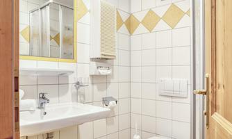 A small bathroom with white tiles and yellow accents. There is a sink, a toilet, and a mirror.