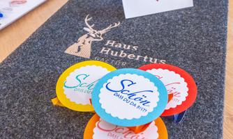 On the table are colorful cards and a menu folder with the logo "Haus Hubertus". A small card with heart motifs is also placed on it.