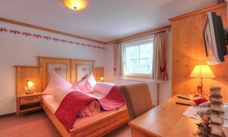 A cozy bedroom with wooden furniture and two single beds. The room has a bright atmosphere and a view of nature.