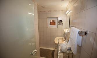 A modern bathroom with tiled walls. It features a shower cubicle, a sink, and a large mirror.