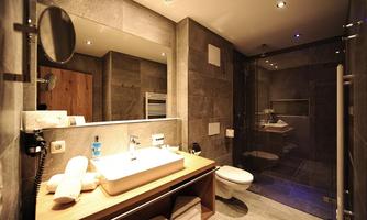 A modern bathroom with gray tiles and elegant fixtures. It features a shower, a sink, and a wooden panel.