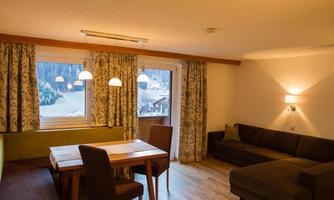 A cozy living space with a table and chairs. Large windows let in plenty of light and provide a view of nature.