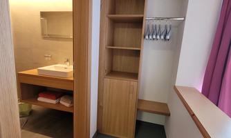 A modern room with a built-in wardrobe and a small seating area. In the background, a bathroom area with a sink and mirror is visible.