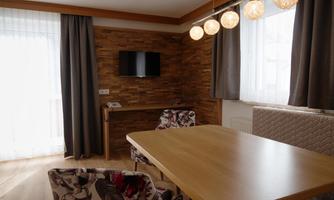 A modern dining room with wooden walls and a large window front. The table is made of wood and there are cozy chairs with floral patterns.