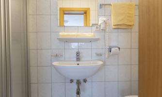 A simple bathroom with a sink, a towel, and a mirror. The walls are covered with white tiles.
