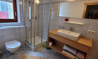 A modern bathroom with a glass shower and an elegant vanity. The walls are tiled and there is a large mirror as well as a towel shelf.