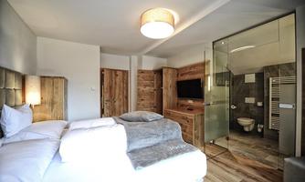 A modern hotel room with a double bed and a cozy sleeping area. In the background, there is an elegant bathroom with a glass shower and toilet.