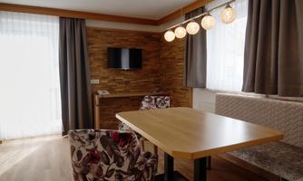 A cozy dining area with a wooden table and floral patterned chairs. Large windows let in plenty of light and modern lighting creates a pleasant atmosphere.
