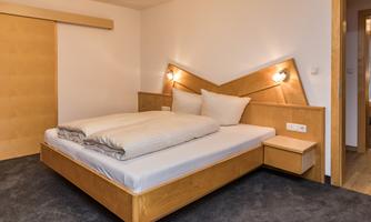 A modern bedroom with a double bed and light wood design. The walls are simple, and the lighting creates a relaxed atmosphere.