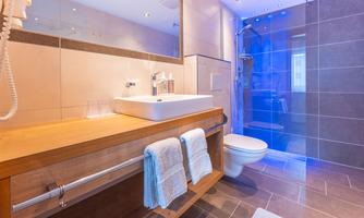 A modern bathroom with an elegant wooden shelf. It features a shower, a sink, and a stylish tile arrangement.