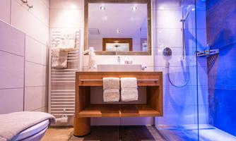 A modern bathroom with a wooden washbasin and two towels. There is a shower and pleasant lighting.