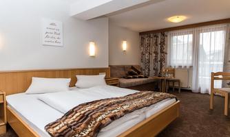 A cozy hotel room with a double bed and a sofa. A large window provides plenty of daylight.