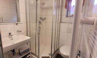 A modern bathroom with a shower cubicle, sink, and toilet. The walls are tiled, and there is a large mirror.
