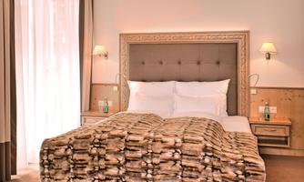 A cozy bedroom with a large bed and a stylish duvet. The brightness from the large windows creates a pleasant atmosphere.