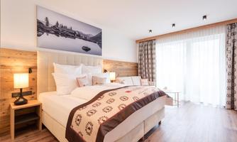A stylish bedroom with a large bed and warm wood decor. Large windows provide plenty of daylight.