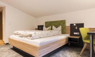 A modern bedroom with a cozy bed and a simple, stylish decor. Next to the bed is a small table with a chair.