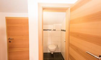 A look at a small toilet with white tiles and a modern toilet. The wooden doors provide a warm contrast to the room.