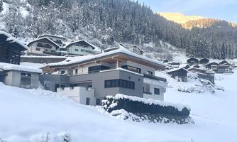 A modern house in a snowy landscape. Surrounded by mountains and traditional chalets, the scene is peaceful and wintry.