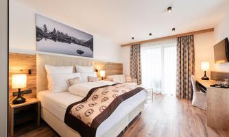 A modern bedroom with a large double bed and a cozy seating area. The large window front ensures plenty of daylight.