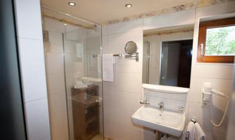 A modern bathroom with a transparent shower cabin and a sink. The walls are tiled in a light color and there is a window that lets in daylight.