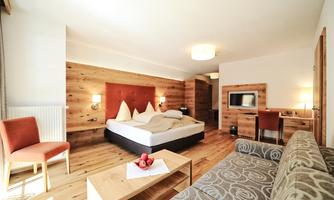 A modern hotel room with wooden elements and a comfortable bed. The room features a television, a desk, and a cozy seating area.
