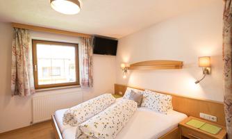 A cozy bedroom with a double bed and light wood interior. Windows and soft lighting create an inviting atmosphere.