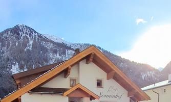 A charming house with a snow-covered mountain in the background. The sun is shining, and the sky is clear and blue.