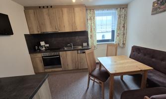 A cozy kitchenette with wooden furniture and a dining table. The room feels bright and inviting.