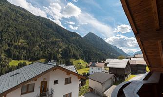 A picturesque mountain landscape with green meadows and tall mountains in the background. In the foreground, traditional alpine houses can be seen.