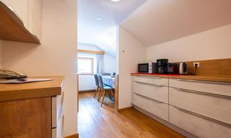 A modern kitchen with wooden flooring and many appliances. In the background, there is a dining area with a table and chairs.