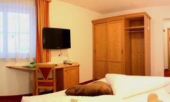A cozy hotel room with a double bed, a desk, and a television. The windows are adorned with curtains and the room has a warm color tone.