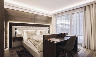 A modern bedroom with a large bed and a beautiful desk. Large windows let in plenty of light and create a bright atmosphere.