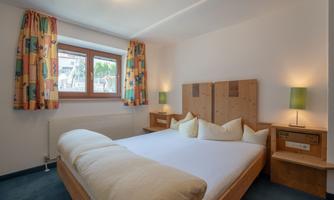A cozy bedroom with a large bed and colorful curtains. There are nightstands and lamps for a pleasant atmosphere.