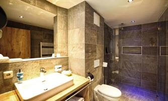A modern bathroom with gray tiles and an elegant sink. The shower is generously designed and the lighting creates a pleasant atmosphere.