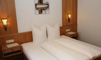 A cozy bedroom with a double bed and modern wooden furniture. The walls are plain and equipped with modern light sources.