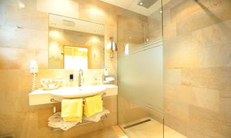 A modern bathroom with a sink, a large mirror, and a glass shower. The walls are designed with bright, natural stones and yellow towels are ready.