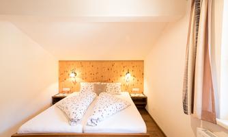 A cozy bedroom with a double bed and two pillows. The walls are brightly and minimally designed, with soft lighting.