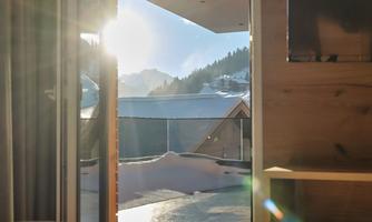 A sunny morning view from a room with a mountain landscape. Light shines in through the open door, creating a cozy atmosphere.