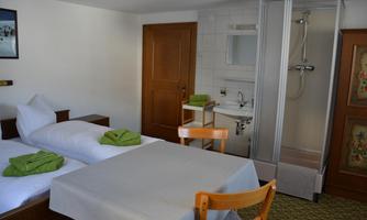A simple room with two single beds and a table. A shower tray and washbasin are visible in the background.