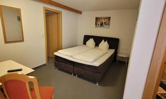 A cozy room with a double bed and a chair. There is a mirror and decorative pictures on the walls.