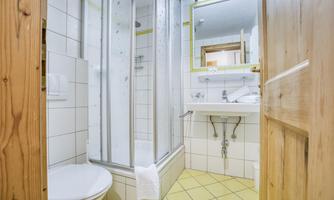 A modern bathroom with a shower, a sink, and a toilet. The walls are tiled and the floor has light tiles.