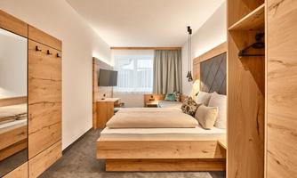 A modern bedroom with wooden furniture and a large bed. The room is bright and inviting, with a window and a cozy design.