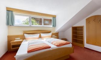 A cozy bedroom with a double bed and orange pillows. There are large windows and storage space in the room.